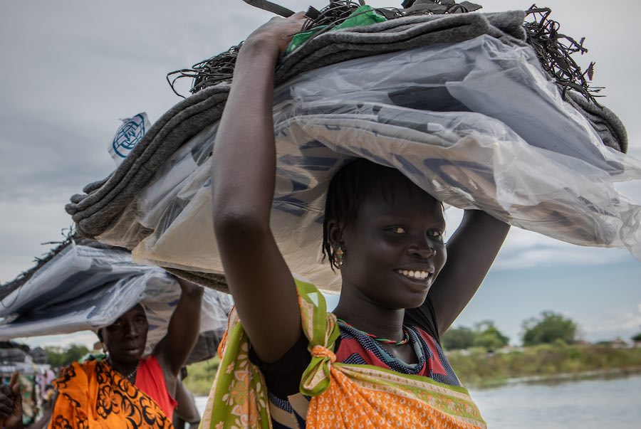 Community members carry a load of non-food items, such as blankets and tarpaulin, distributed by NGOS, following devestating flooding, in Pibor, Boma State, South Sudan, on 6 November 2019 // Photo credit: UNICEF South Sudan/de la Guardia