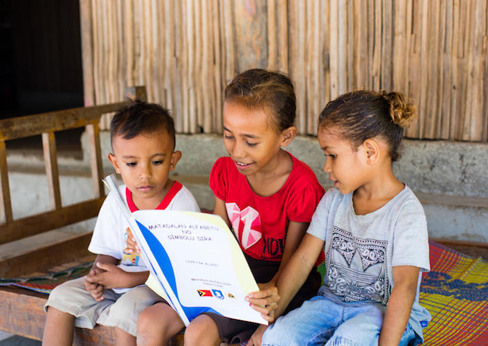 On April 14, 2020, a girl reads as children look on in Timor-Leste after the country's schools shut down to prevent the spread of COVID-19. 