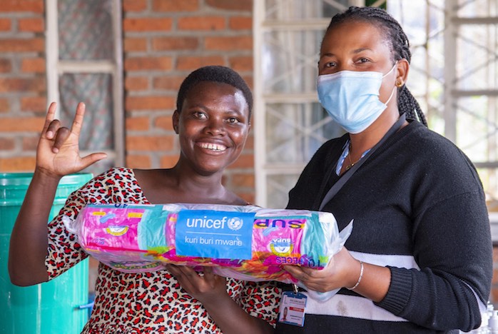 Marie, 20 (left), poses with the supply distributor and new packages of menstrual pads procured and delivered by UNICEF.