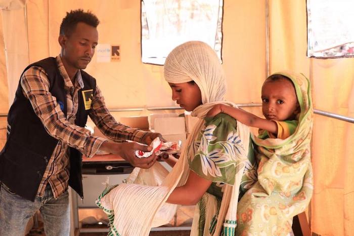A mobile health worker gives therapeutic food packets to a mother whose child is suffering from severe acute malnutrition at the UNICEF-supported Mai Tsebri site for families displaced by fighting in Ethiopia's Tigray region.