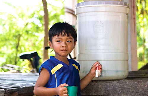 A boy stands with a ceramic filter by a water pump in Cambodia. 