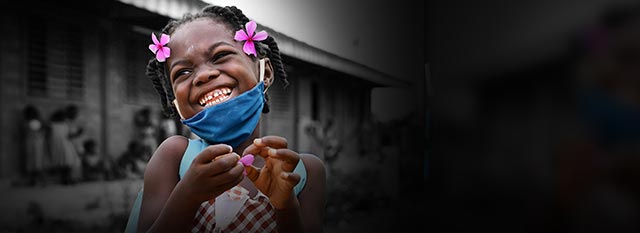 A girl wearing a face mask smiles in front of her school