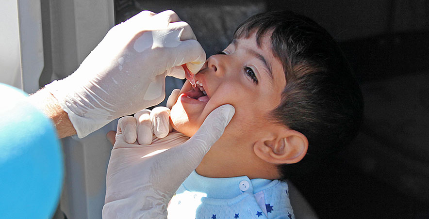 a child receives an oral immunization from an adult in PPE