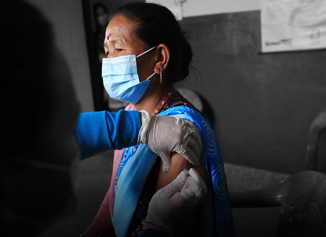 a senior woman in a face mask receives a vaccine from someone wearing PPE