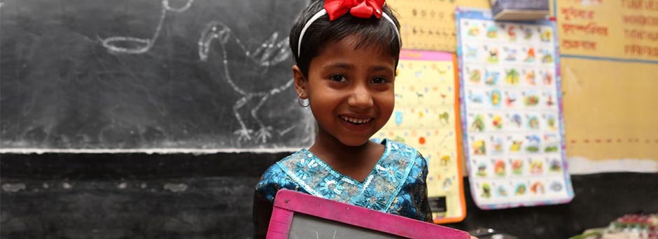 A girl holds a slate in a classroom in Bangladesh