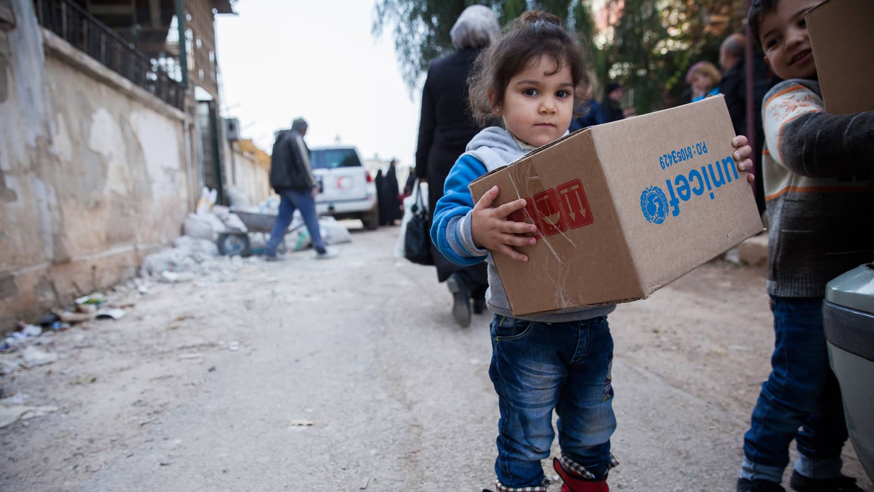  A young girl in Al-Waer, Homs, Syria, carries a box of winter clothes provided by UNICEF.