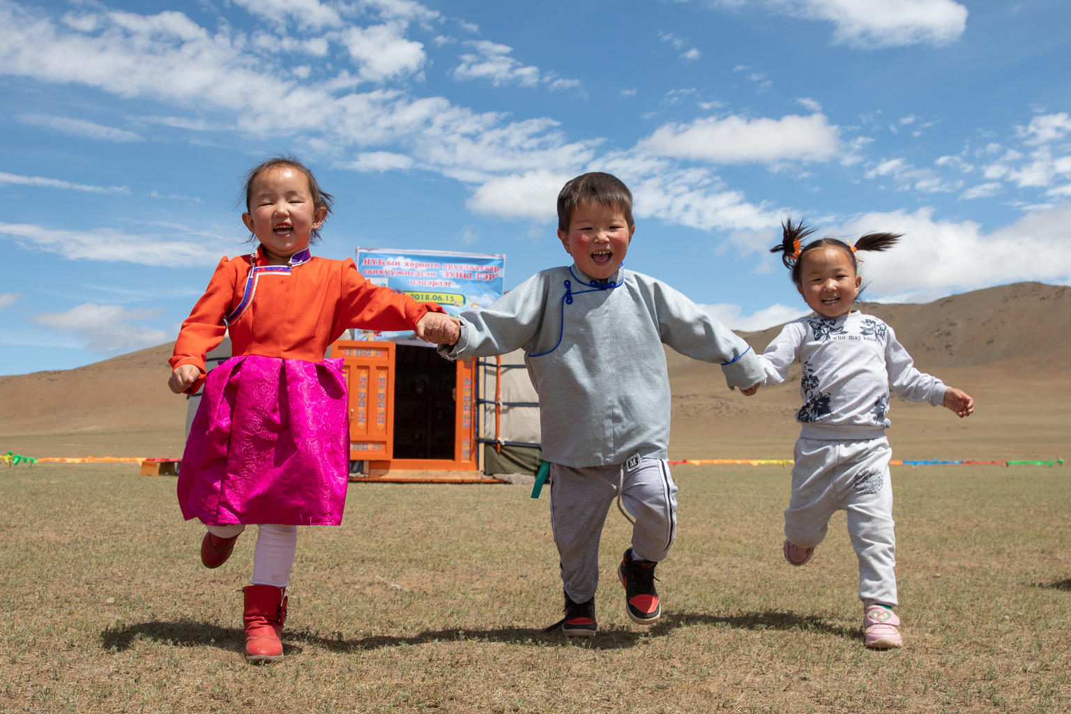 On June 17, 2018, in Mongolia, three laughing children run hand-in-hand outside the newly opened mobile ‘ger’ (traditional nomadic tent) kindergarten.