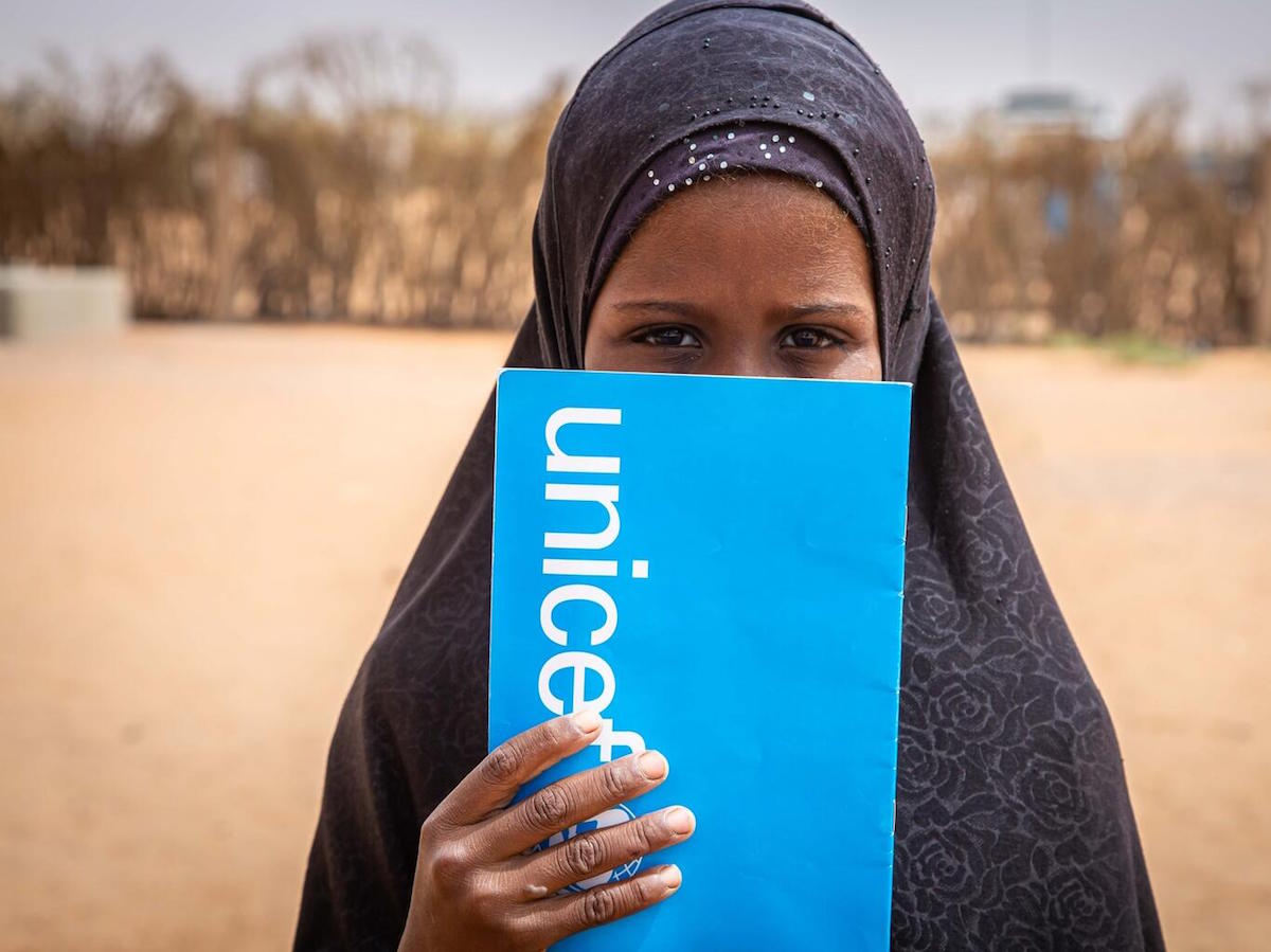 A student peeks out from behind her UNICEF notebook in Mbera refugee camp in southeastern Mauritania in 2021.