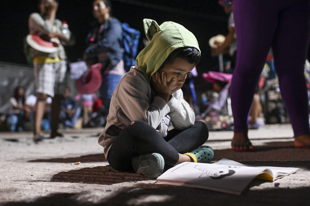 A child migrant sits on the floor with a coloring book.