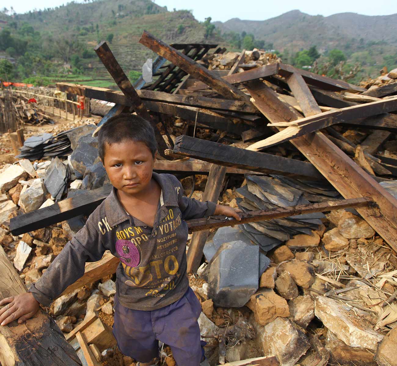 A young boy stands on the rubble of a destroyed home in central Nepal. Donation Form Background