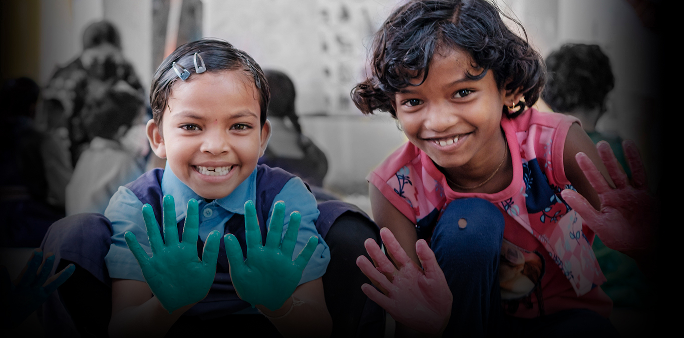 Two children smile and hold out their hands that are covered in paint