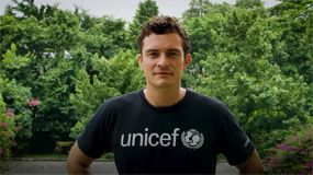 Orlando Bloom stands in front of trees wearing a UNICEF t-shirt