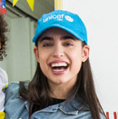 Sofia Carson smiles at the camera while wearing a blue UNICEF baseball cap