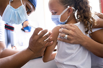 A health care worker in P.P.E. gives a shot to a young girl in her arm