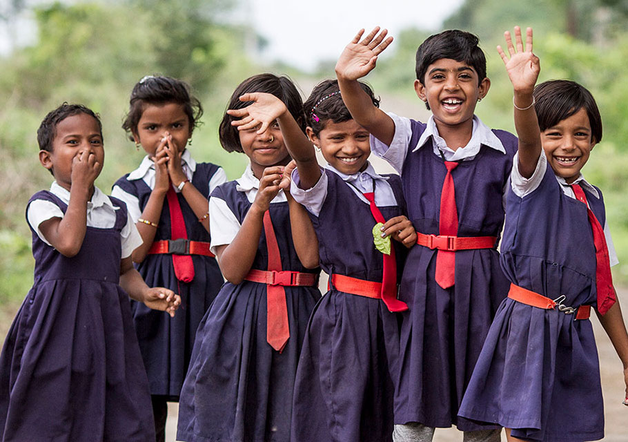 A group of Indian school girls wave to the camera while standing outside.