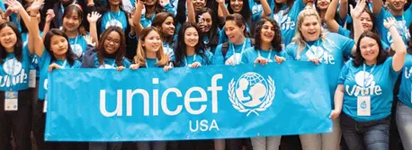 Group of teens/young adults in light blue UNICEF t shirts. The front row is holding up a matching light blue banner that said UNICEF USA