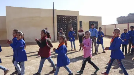 14 children smiling and playing outside in a sunny enclosed area.
