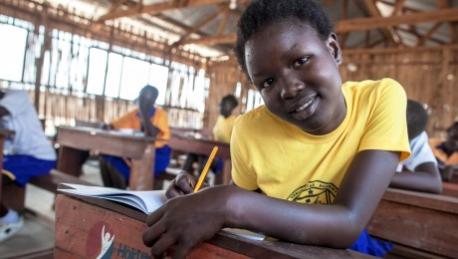 African child sitting at a desk in school with a book open. Smiling and looking at the camera