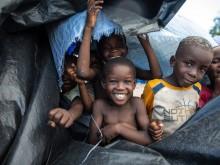 Four young boys smile and play in a pile of junk and trash. 