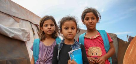 Three girls with UNICEF backpacks stand outside a tent school at the Junaina makeshift camp in northern rural Idlib, Syria.