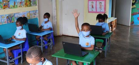 In a primary school classroom in Hartcliffe, Harare, Zimbabwe, a boy, his hand raised, sits at a desk with a laptop loaded with lessons from the Learning Passport.