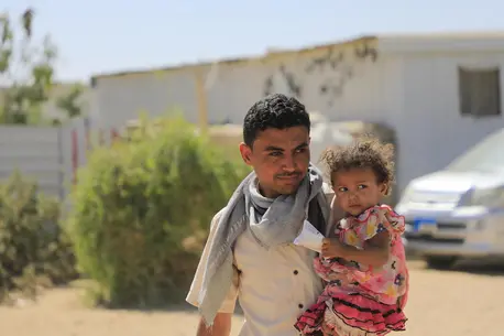 In 2022, a father holds his 2-year-old daughter outside the family's home in a camp for internally displaced families in Yemen's Marib governorate.