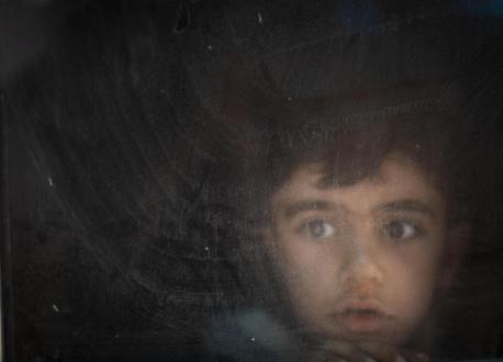 child peering out a window in a darkened room