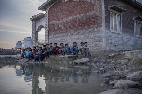 Children sit beside a lake of contaminated floodwater near Zangi Brohi Village, Dadu District, Sindh