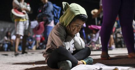 A child migrant sits on the floor with a coloring book.