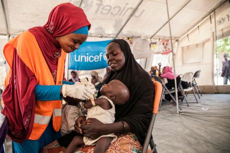 UNICEF Nutrition Officer, Aishat Abdullahi, assesses 7-month-old Umara Bukar for malnutrition at a UNICEF-supported health clinic at Muna Garage displacement camp, Maiduguri, Borno State, northeast Nigeria as Umara’s mother (in black) looks on.