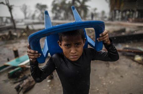 In Bilwi, Nicaragua, a young boy holds a plastic chair over his head to shield himself from pelting rain while standing in the spot where his house used to stand until it was destroyed by Hurricane Iota.