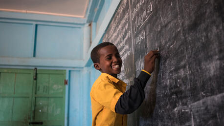 A student laughs as he writes the answers to questions on the chalkboard of his classroom in the UNICEF-supported Salaama primary school in Galkayo, Somalia,.