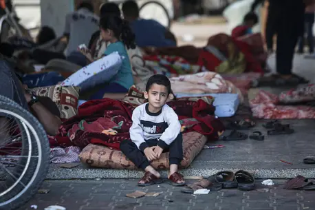 Ahmad, 5, sits on his mattress in a shelter courtyard in Gaza, surrounded by hundreds of other displaced people.