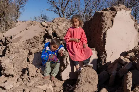 On Dec. 3, 2023, children sit for a portrait on a pile of rubble where their home used to stand in earthquake-affected Zinda Jan district, Herat province, Afghanistan.