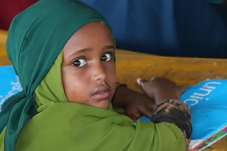 In Somalia, a young girl sits at a desk with her workbook and pencil at a UNICEF-supported temporary learning center for children displaced by severe drought.