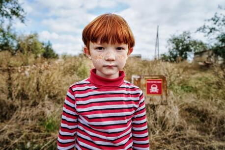 Leonid, 6, stands in front of a sign that reads "Danger of Mines" in the Kharkiv region of Ukraine.