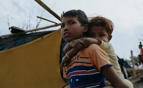 Rafiq, 14, holds his little sister in front of their temporary shelter at the Rohingya refugee settlement in Cox's Bazar, Bangladesh.