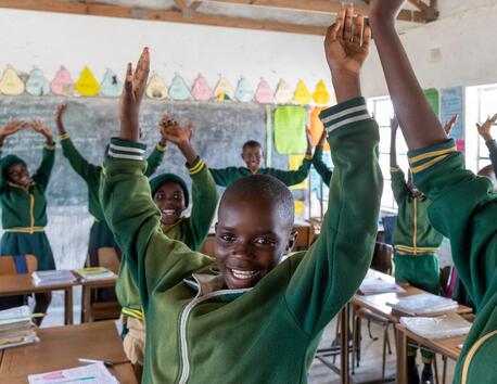 Students at UNICEF-supported Mapengani Primary school in Matebeleland South Province, Zimbabwe, smile and stretch their arms overhead during a classroom activity.