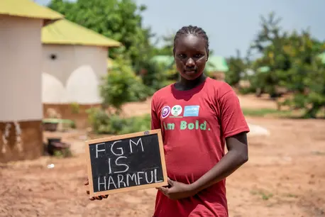 A girl in The Gambia holds a sign protesting against female genital mutilation.