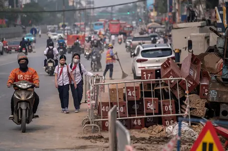 People wearing masks navigate through a dusty construction area on Kim Dong Street, Hai Ba Trung District, Hanoi, Vietnam.