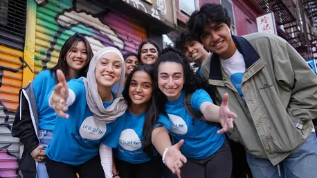 A group of smiling UNICEF club members wearing UNICEF T shirts stand in front of a mural.