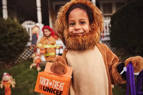 Kid in lion costume holding little orange box trick-or-treating for UNICEF.