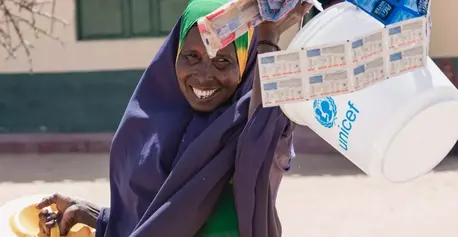 A woman carries a UNICEF WASH kit containing items she selected through a token system.