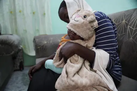 Raped by armed men in Khartoum at the age of 17, a young woman holds her baby son on her lap.