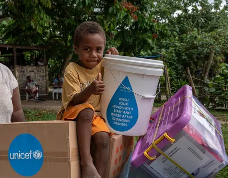 Four-year-old Johnathan sits holding items included in an emergency kit distributed by UNICEF and partners to earthquake-affected families in Erakor Bridge Community in south Efate, Vanuatu, in December 2024.