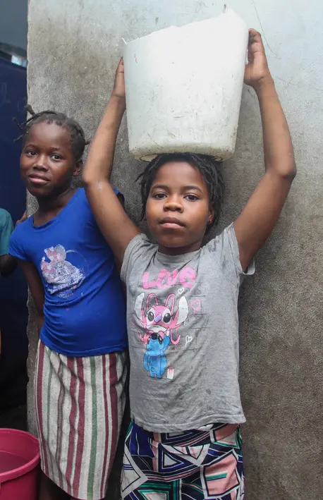 Two displaced children in Port-au-Prince, Haiti, carry buckets of water.