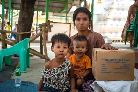 On March 31, 2025, a woman with two small children poses for a photograph with a box of UNICEF hygiene kits distributed to earthquake survivors in the Sagaing region of Myanmar.