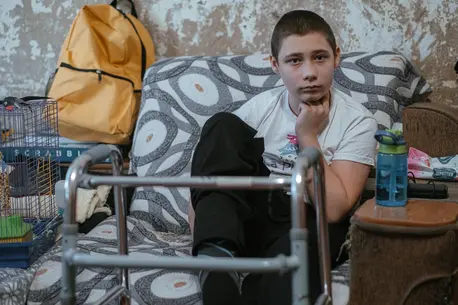 In Nikopol, Kharkiv oblast, eastern Ukraine, Nazar, 13, sits in his family's living room, his walker nearby. His legs and feet were injured by an explosive remnant of war. 