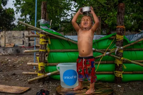 On April 6, 2025, a boy bathes beside a temporary water tank made with tarpaulin provided by UNICEF at a makeshift tent camp in Amarapura township, Mandalay region, Myanmar, following the recent earthquake.
