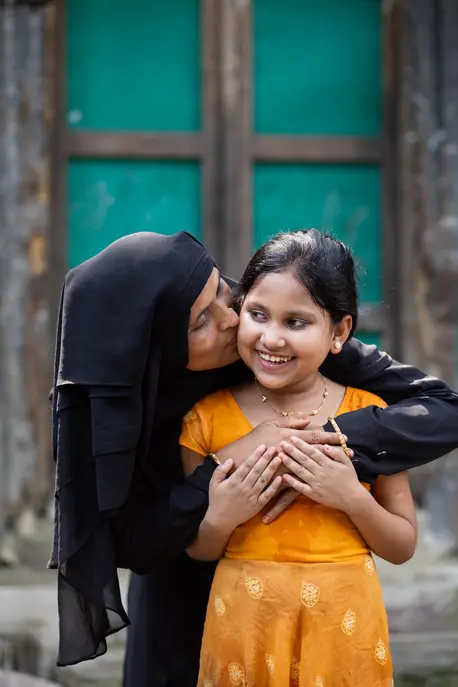 A mother hugs and kisses her smiling daughter in Bangladesh. 
